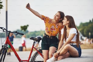 Making a selfie. Two young women with bike have a good time in the park.