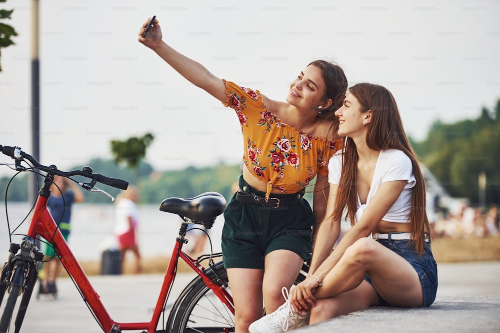 Making a selfie. Two young women with bike have a good time in the park.