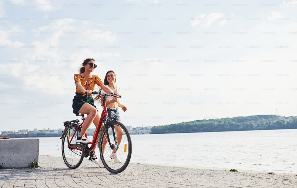 Menina corre perto de bicicleta. Duas amigas na bicicleta se divertem na praia perto do lago.