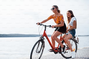 Two female friends on the bike have fun at beach near the lake.