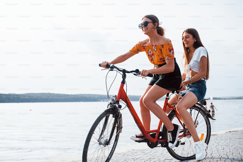 Duas amigas na bicicleta se divertem na praia perto do lago.