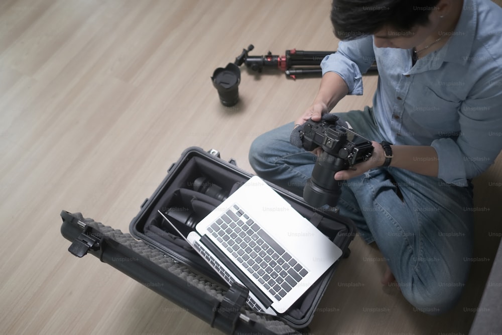Photographe professionnel assis sur un plancher en bois et ajuste l’appareil photo.