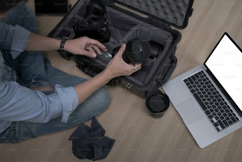Photographer sitting on wooden floor and putting camera accessories in special bag.