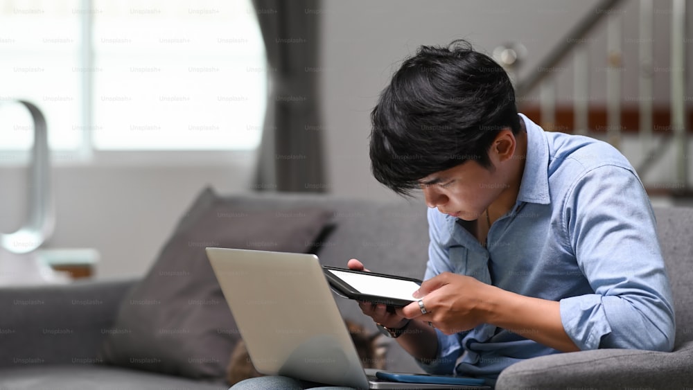 Homme d’affaires travaillant en ligne sur un ordinateur portable et utilisant une tablette numérique à la maison.