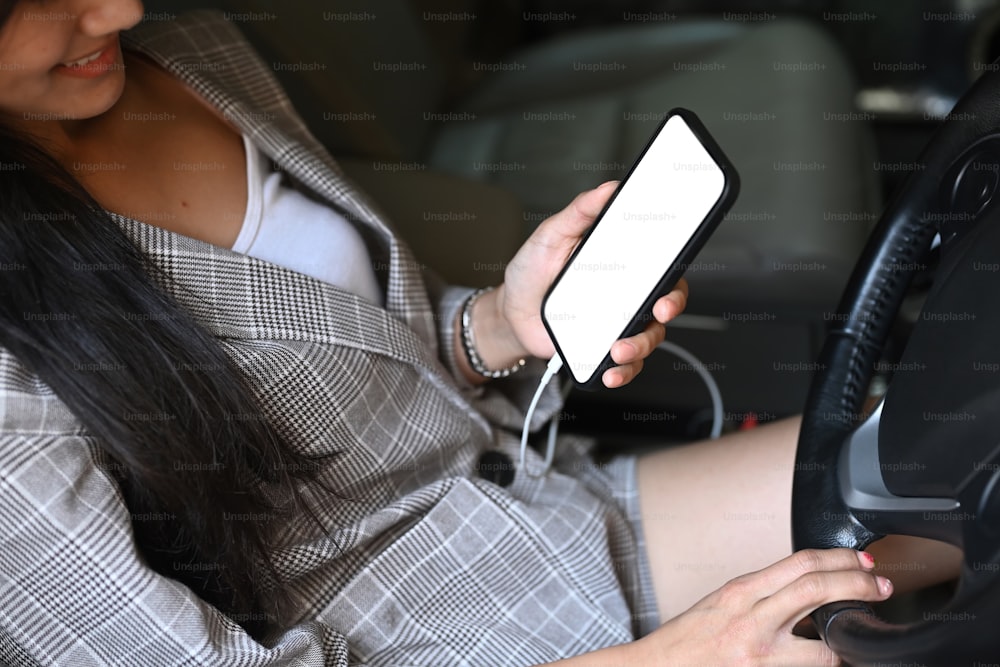 Junge Geschäftsfrau hält Smartphone während der Autofahrt.