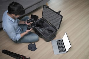 Vista de ángulo alto del fotógrafo masculino sentado en el piso de madera y colocando los accesorios de la cámara en una bolsa especial.
