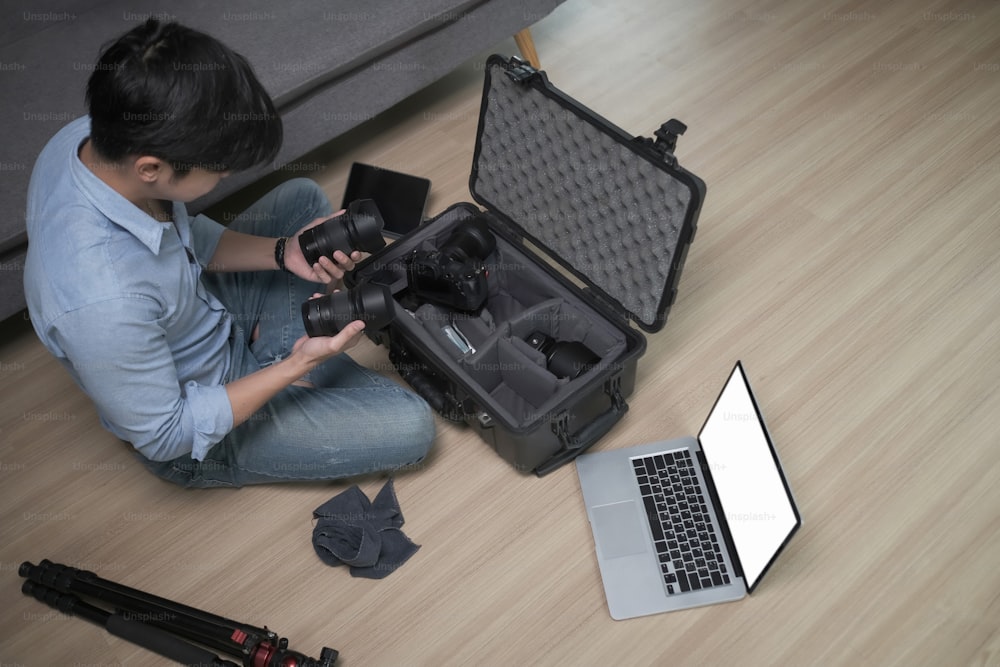 Hight angle view of male photographer sitting on wooden floor and putting camera accessories in special bag.