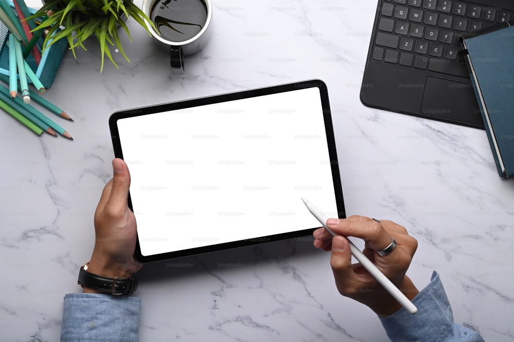 Top view of man hands holding stylus pen and digital tablet with empty screen on marble background.