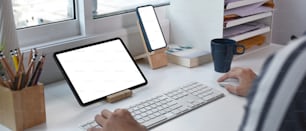 Immagine orizzontale di un giovane che lavora online con più dispositivi nell'ufficio di casa.
