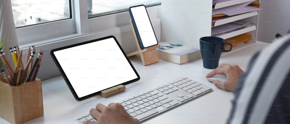 Imagem horizontal do jovem trabalhando on-line com vários dispositivos em home office.