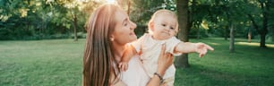 Mothers Day holiday. Young smiling Caucasian mother and boy baby toddler son hugging in park outdoors. Happy authentic family childhood lifestyle. Web banner header.
