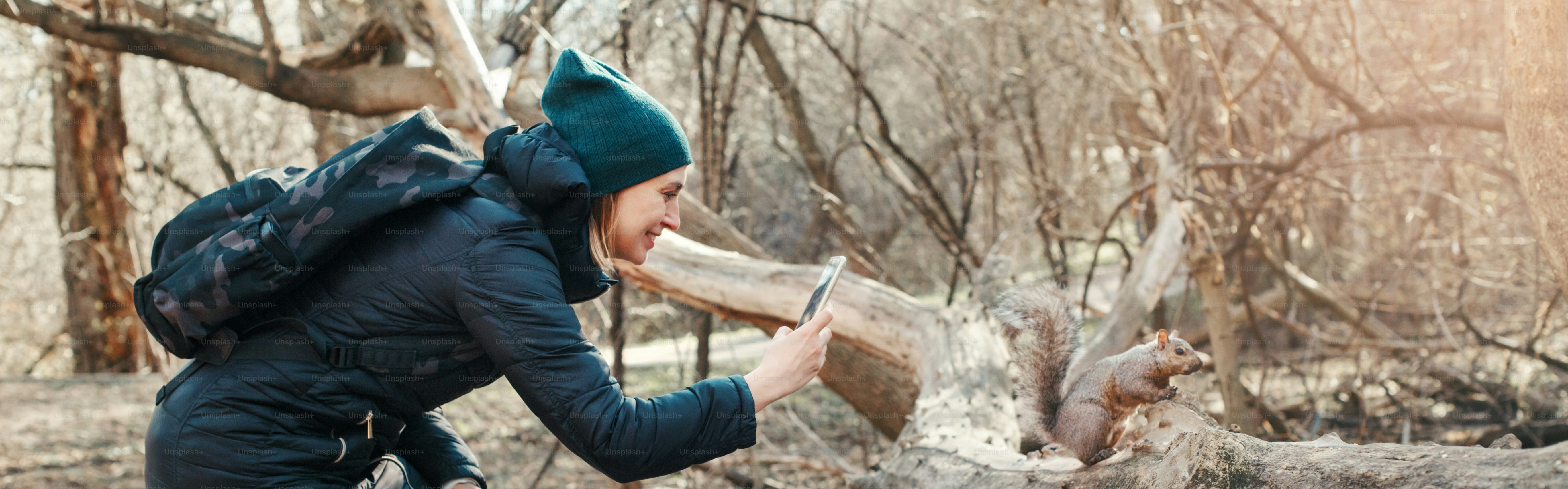 Woman taking picture photo of squirrel in park. Tourist traveler girl snapping smartphone photos of wild animal in forest. Fun outdoor activity and blogging vlogging online. Web banner header.