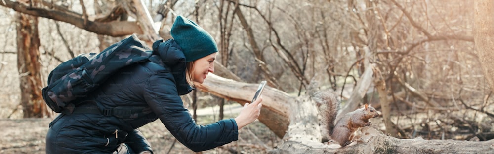 공원에서 다람쥐의 사진 사진을 찍는 여자. 숲에서 야생 동물의 스마트폰 사진을 찍는 관광 여행자 소녀. 재미있는 야외 활동 및 온라인 블로깅 블로깅. 웹 배너 헤더.