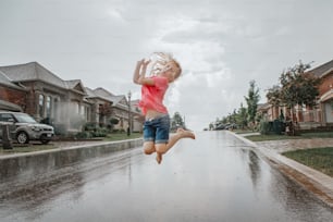 Cute adorable girl running splashing under rain on street road. Child having fun during rain shower storm. Seasonal summer outdoors activity for kids. Freedom and happy childhood lifestyle.
