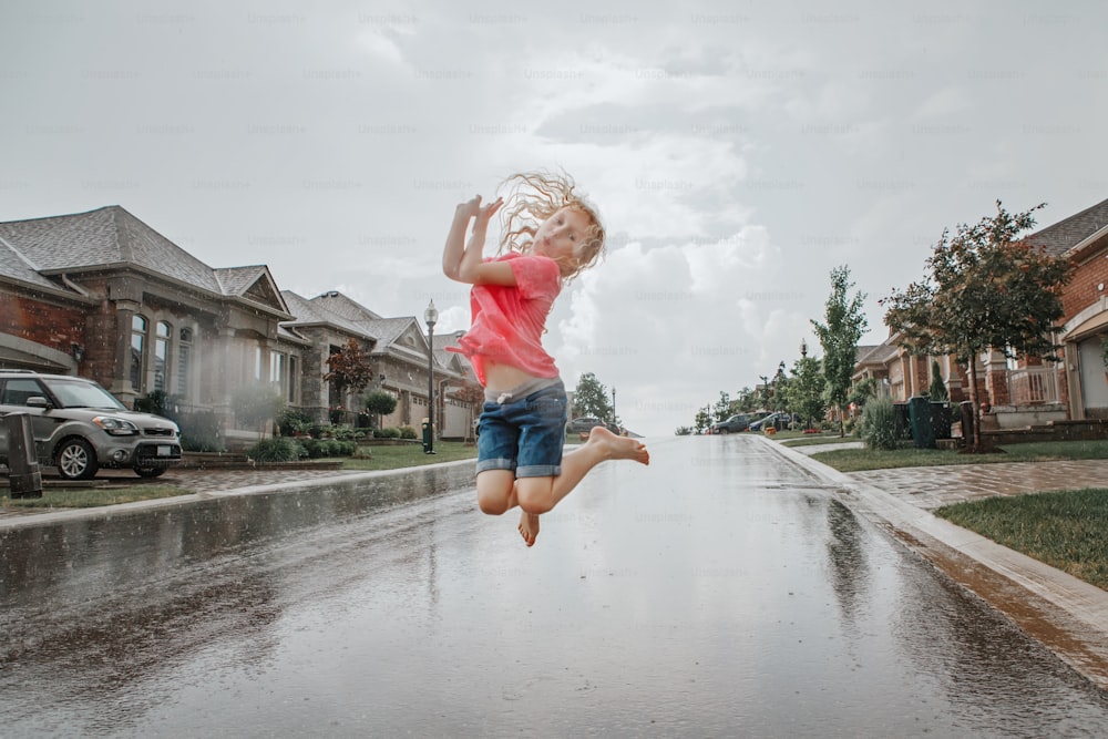 Cute adorable girl running splashing under rain on street road. Child having fun during rain shower storm. Seasonal summer outdoors activity for kids. Freedom and happy childhood lifestyle.