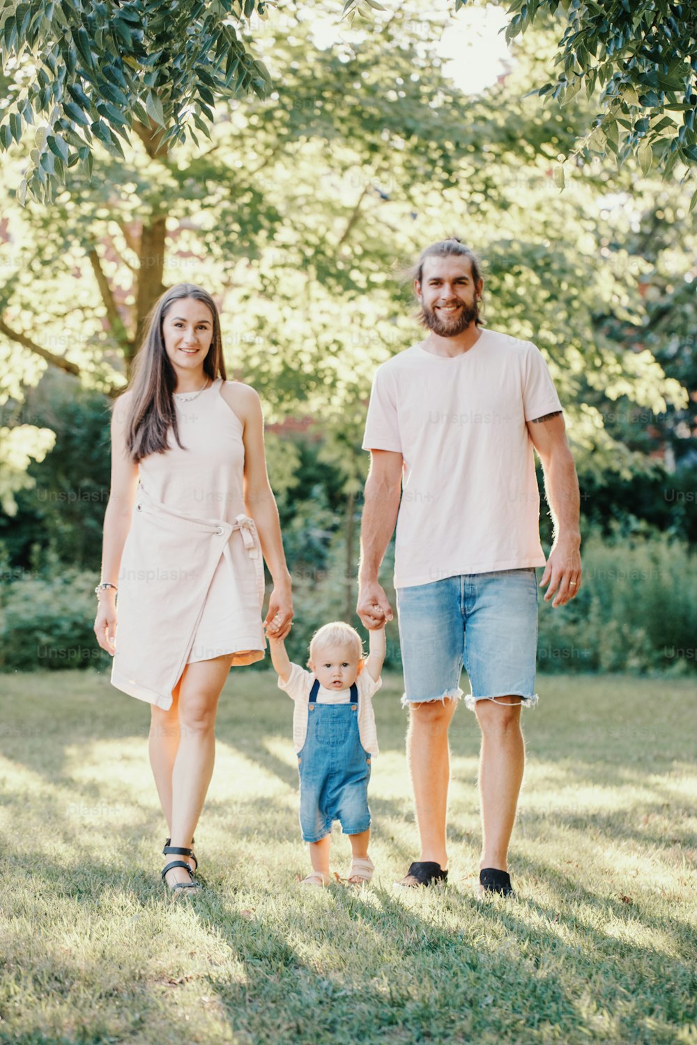 Happy smiling mother and father hold hands with baby boy in park outdoor. Family Caucasian mom and dad with son walking together. Happy family authentic lifestyle concept.