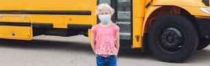 Junge Schülerin mit blauer Gesichtsmaske am gelben Schulbus. Bildung und Rückkehr in die Schule im September. Neue Normalität während Coronavirus Covid-19. Webbanner-Header.