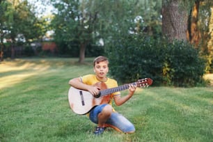 Hard of hearing preteen boy playing guitar outdoors. Child with hearing aids in ears playing music and singing song in park. Hobby art activity for children kids. Authentic childhood moment.