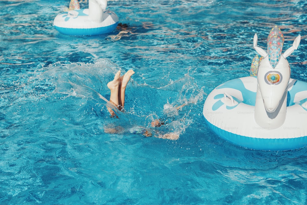 재미 있은 소녀는 풍선 반지 유니콘에서 떨어졌습니다. 수영장에서 즐거운 시간을 보내는 아이. 아이들을 위한 여름 야외 수상 활동. 수영장 물에서 공중에 다리를 올립니다.