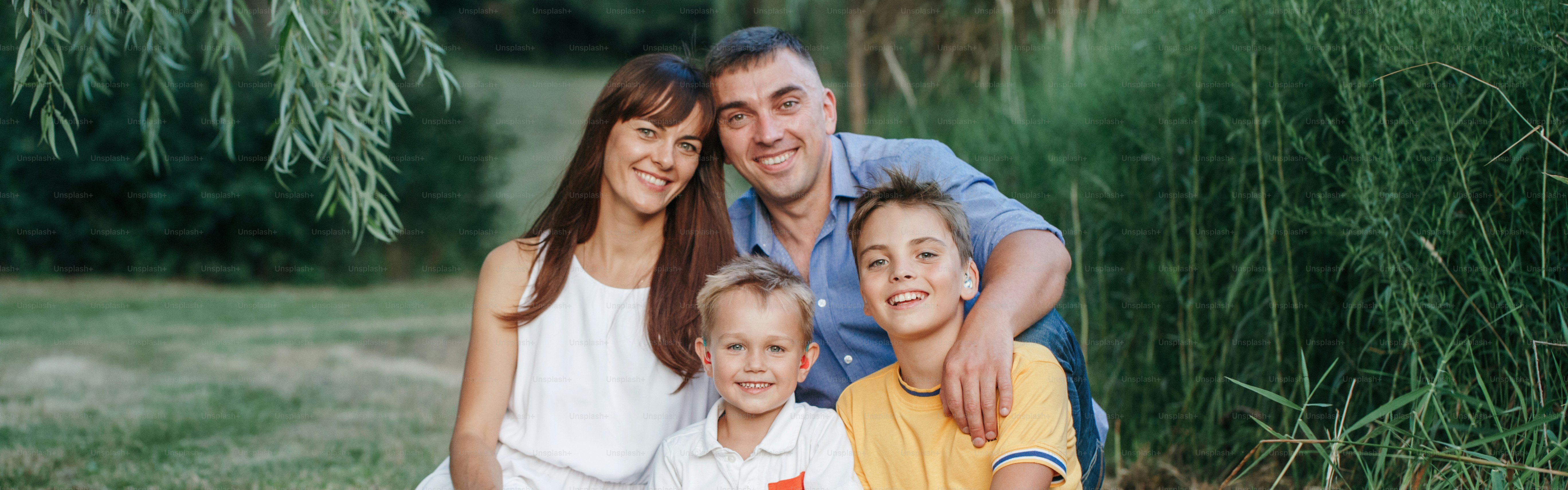 Happy Caucasian family of four people in park outdoors on summer day. Mother and father hugging two sons brothers siblings. Lifestyle authentic natural emotions moment. Web banner header.