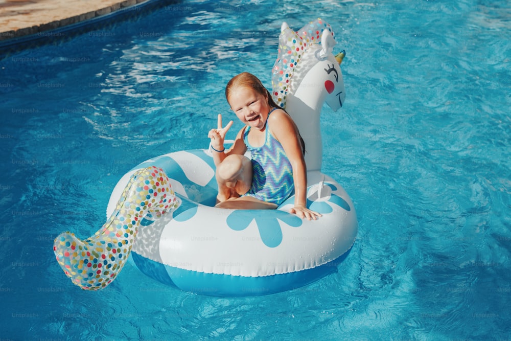 Muchacha pelirroja caucásica sonriente acostada en un unicornio inflable del anillo. Niño disfrutando de divertirse en la piscina. Actividad acuática de verano al aire libre para niños. El tiempo libre y el descanso se relajan al aire libre.