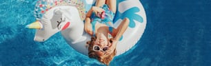 Cute adorable girl in sunglasses with drink lying on inflatable ring unicorn. Kid child enjoying having fun in swimming pool. Summer outdoor water activity for kids. Web banner header.
