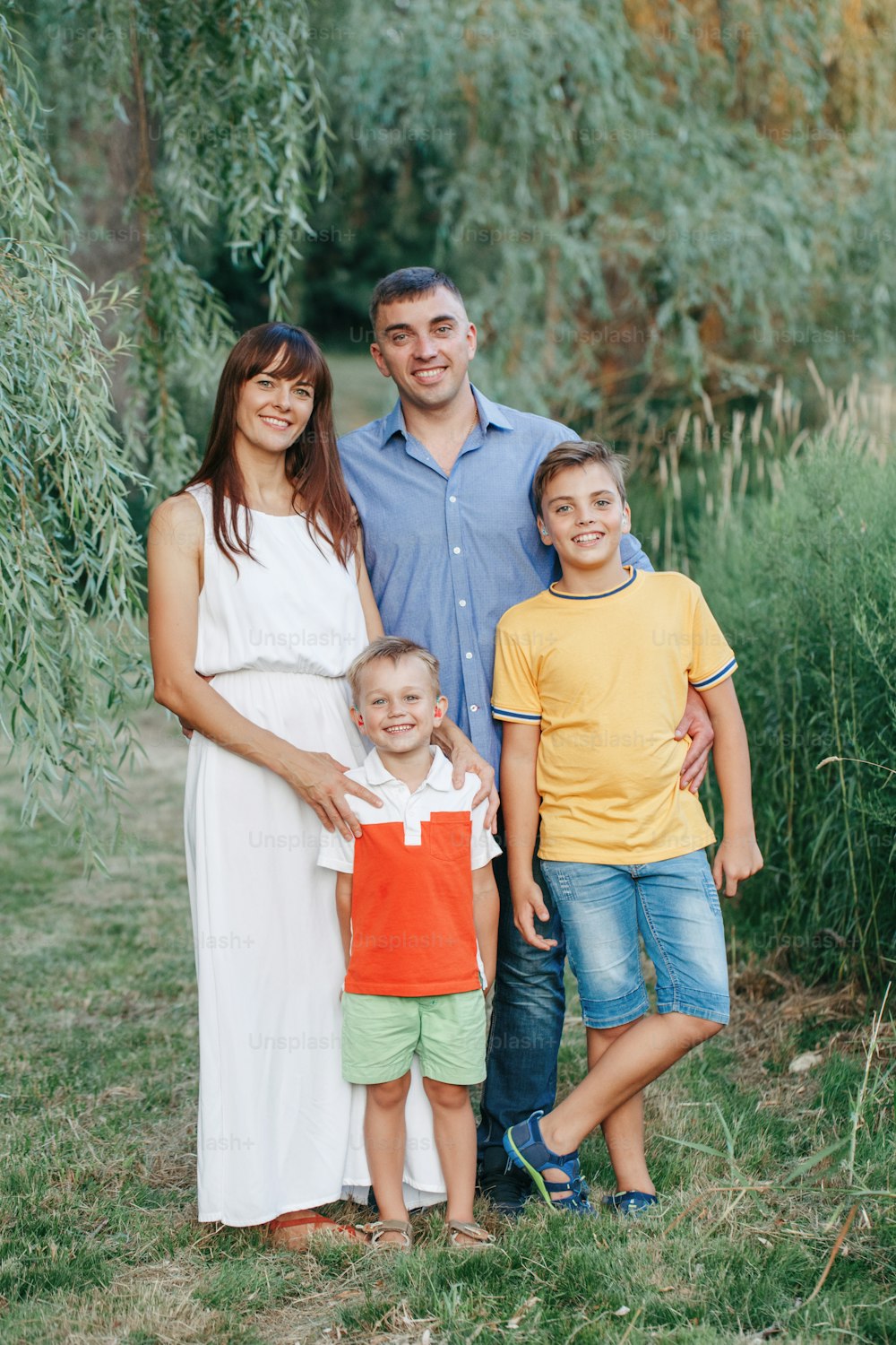 Beautiful happy Caucasian family of four people in park on summer day outdoors. Mother and father hugging two sons brothers siblings. Lifestyle authentic natural emotions moment.