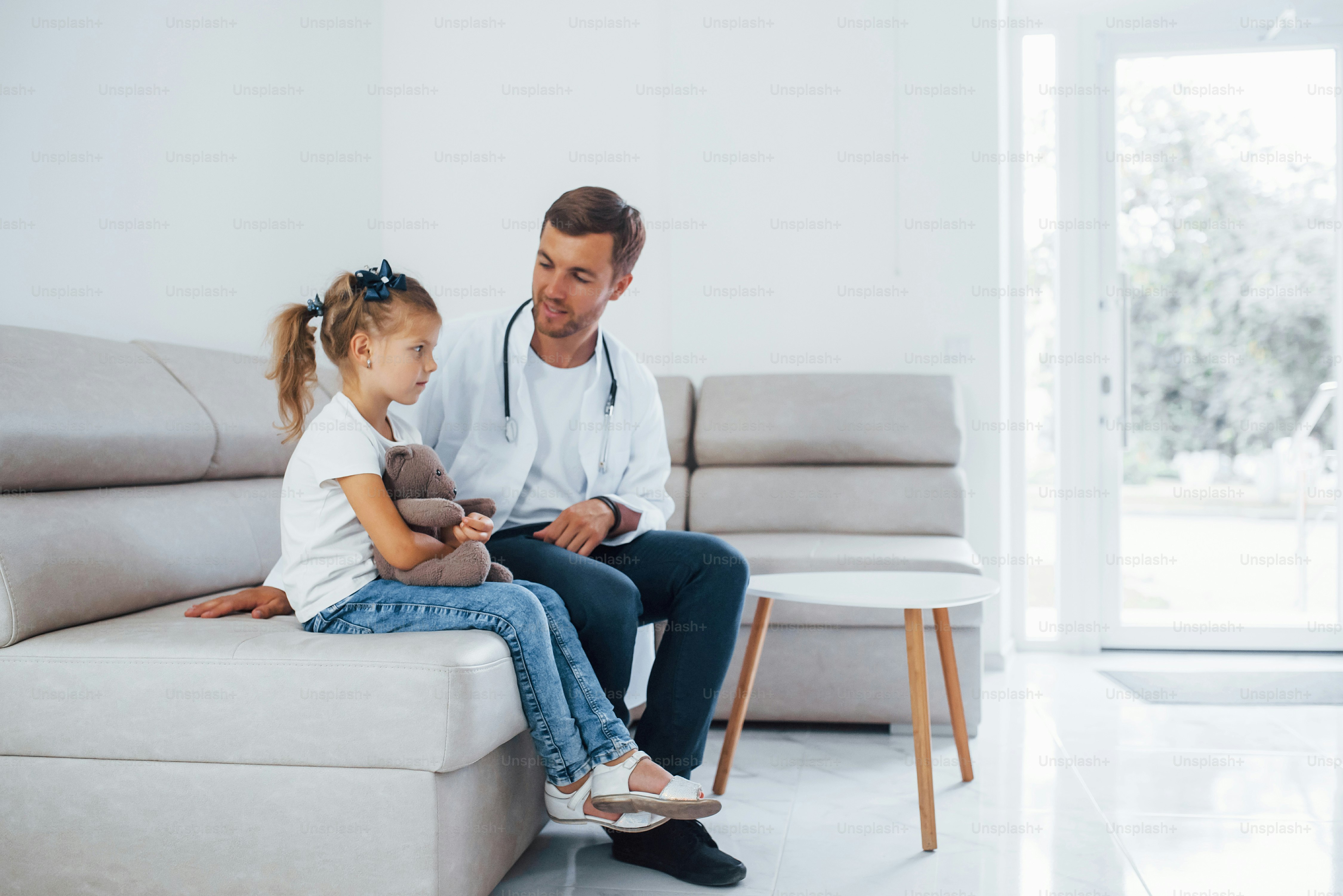 Male doctor in white uniform sits in the clinic with little girl.