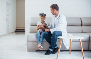 Male doctor in white uniform sits in the clinic with little girl.