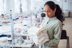 Une couturière se tient dans l’usine avec un tissu dans les mains.