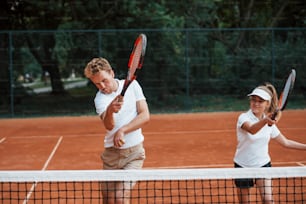 Two people in sport uniform plays tennis together on the court.