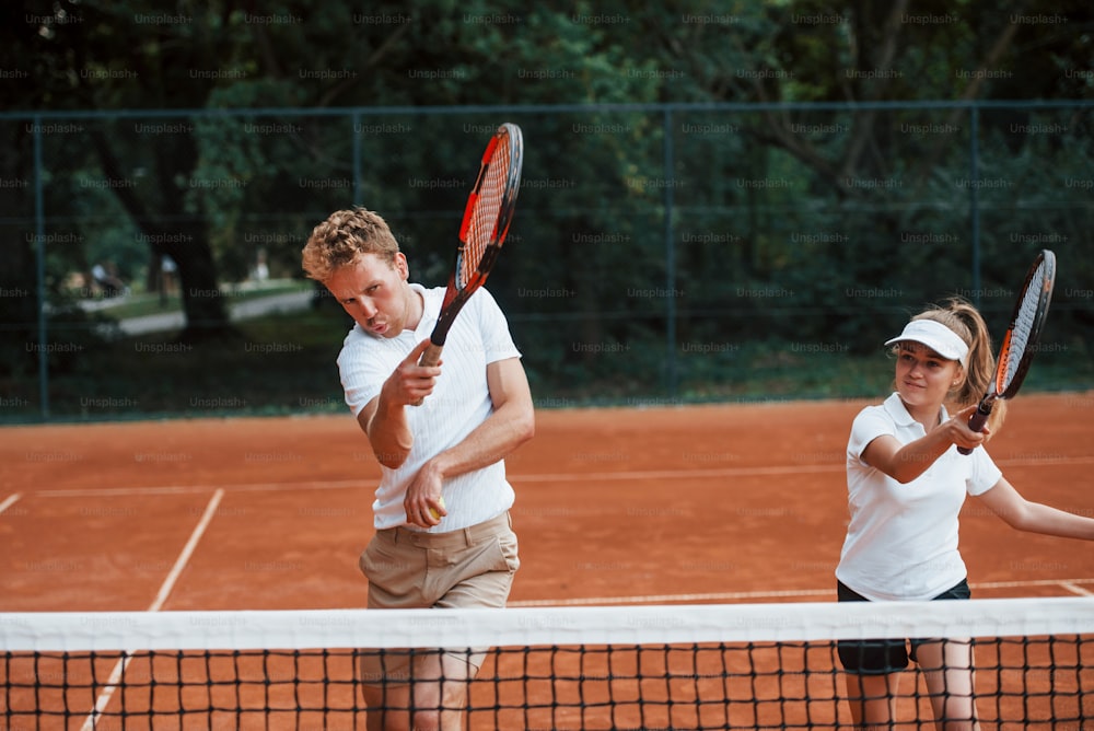 Two people in sport uniform plays tennis together on the court.