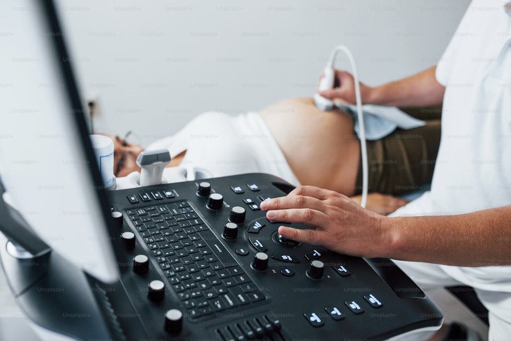Männlicher Arzt macht Ultraschall für eine schwangere Frau im Krankenhaus.