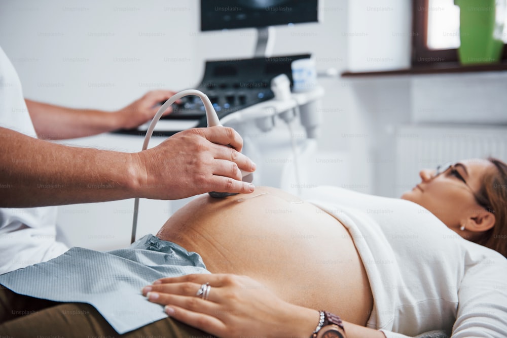 Männlicher Arzt macht Ultraschall für eine schwangere Frau im Krankenhaus.