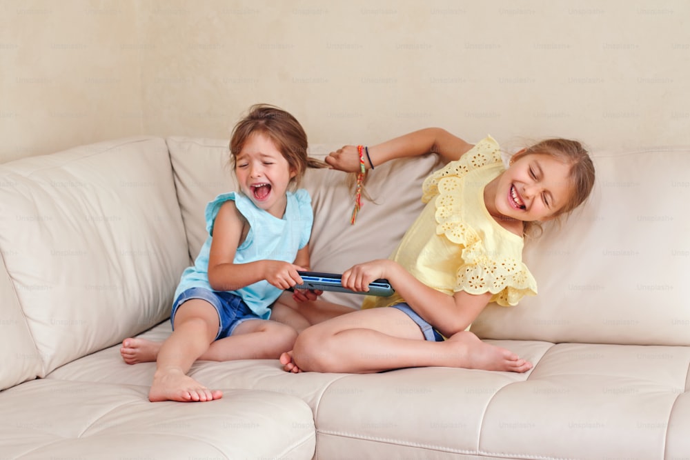 Due piccole sorelle arrabbiate che litigano a casa. Le ragazze amiche non possono condividere il tablet del gadget. Stile di vita autentico divertente momento familiare di fratelli litigano la vita. Cattivo comportamento dei bambini.