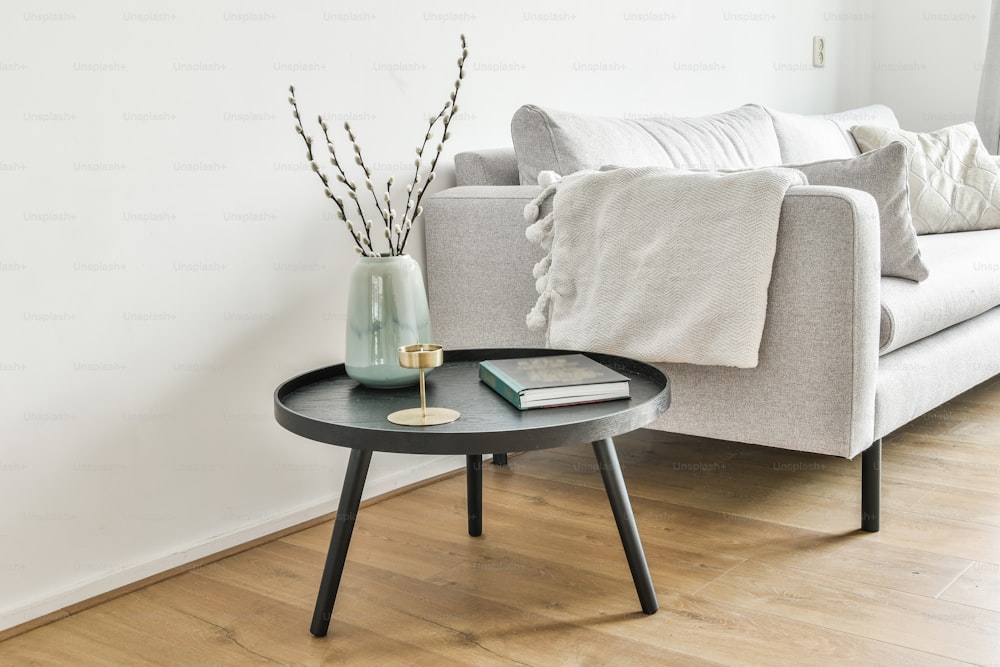 Book, plant pot, candle on a small coffee table by the white sofa