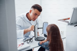 Two panels on the table. Young ophthalmologist is with little female visitor in the clinic.