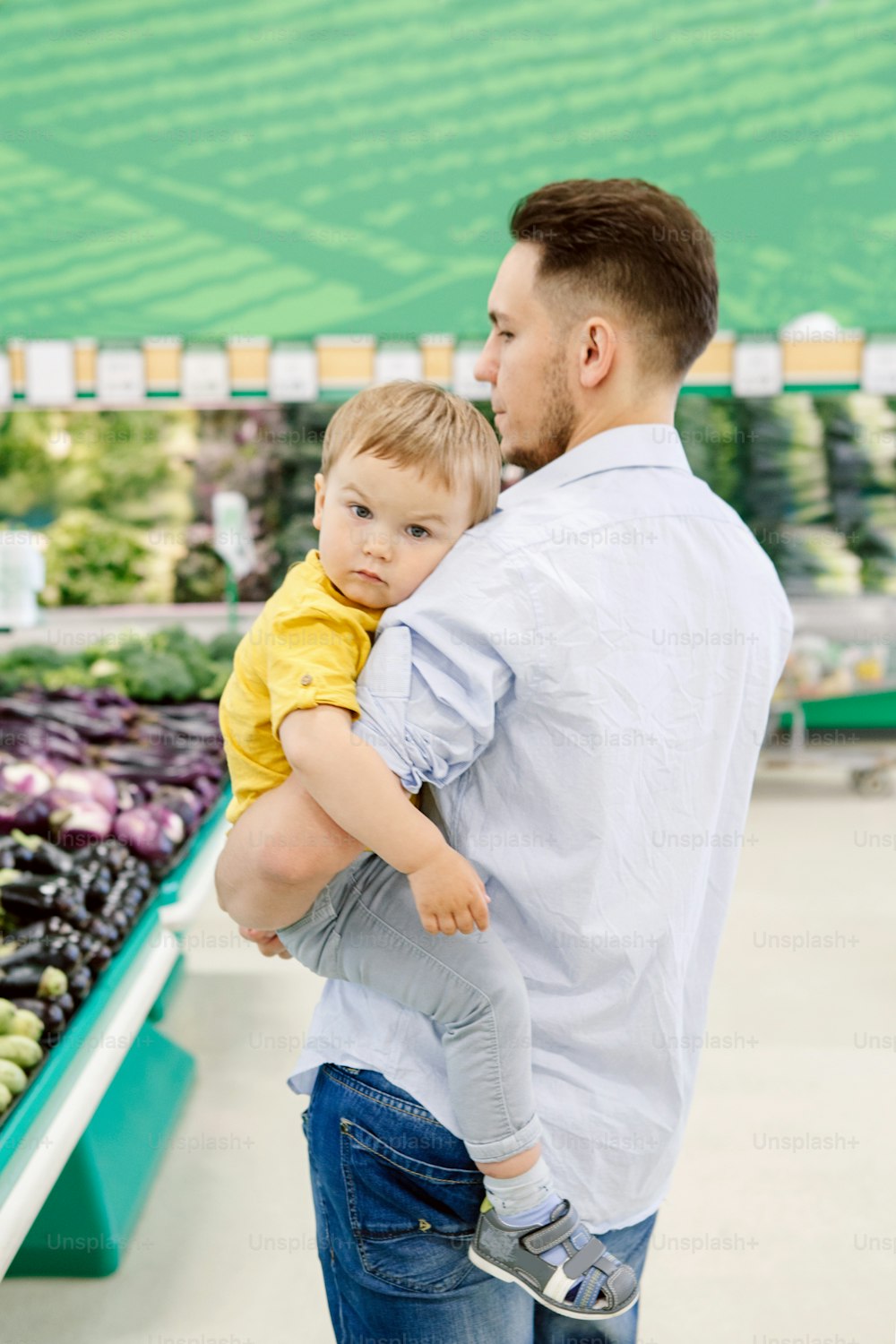 Pai caucasiano fazendo compras no supermercado com o filho bebê. Papai comprando legumes frescos. Pai do homem com criança pequena escolhendo refeição saudável para o almoço do lanche. Estilo de vida autêntico momento sincero.