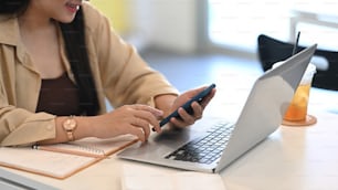 Mujer joven sentada en un café usando un teléfono móvil y trabajando con una computadora portátil.