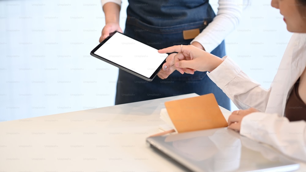 Female waiter accepting orders from customers coming to the coffee shop by using tablet to receive orders.