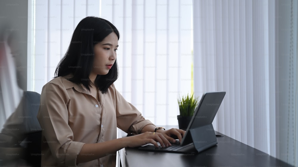 Attractive young woman office worker concentrate working on computer tablet while sitting in office.