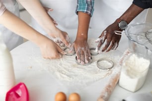 Cropped view of the hands of father, mother and daughter squeeze out the dough using cookie cutters in kitchen at home