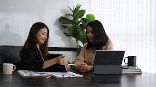 Businesswoman showing business data on digital tablet to her colleague and discussing company financial strategy at office.