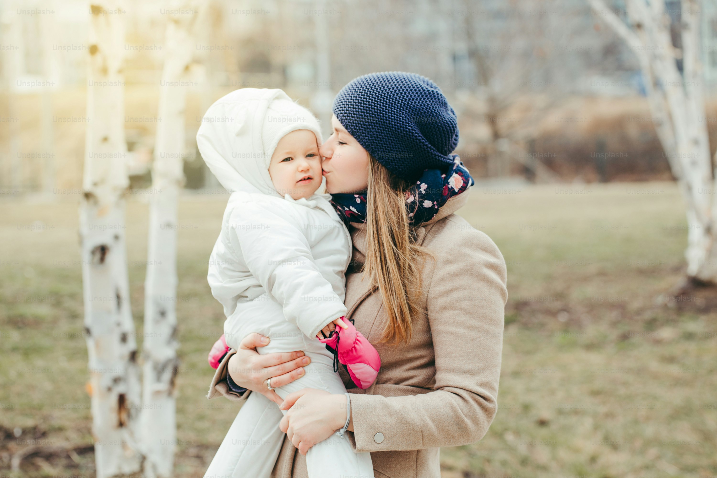 Liburan Hari Ibu. Ibu muda Kaukasia yang bahagia menggendong bayi perempuan di luar ruangan pada hari musim semi. Keluarga dua orang berjalan-jalan bersama di luar. Gaya hidup otentik dengan bayi anak-anak.