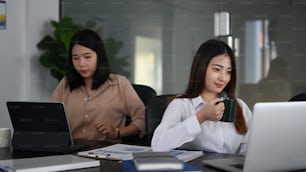 Due donne d'affari fiduciose che lavorano e si siedono insieme in una moderna stanza dell'ufficio.