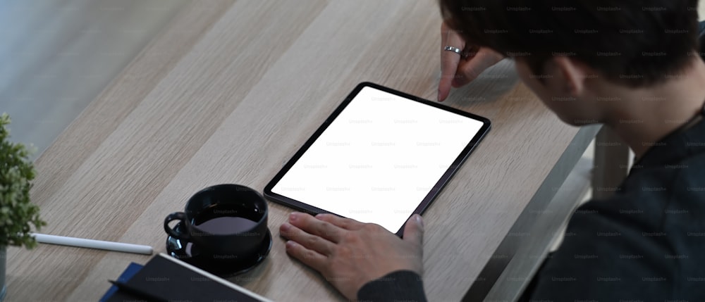 Horizontal image of young man using stylus pen writing on digital tablet while sitting in living room.