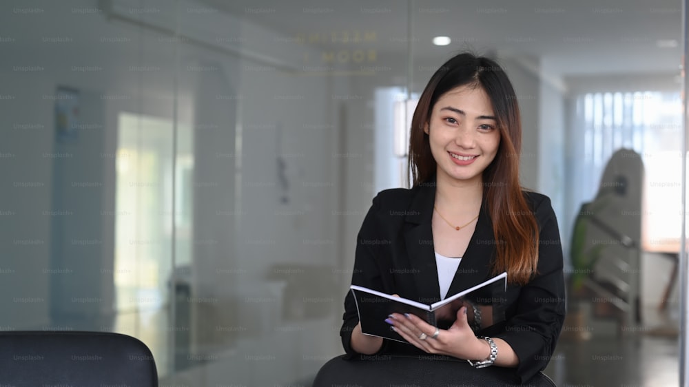 Confident young businesswoman in suit holding folder and smiling to camera.