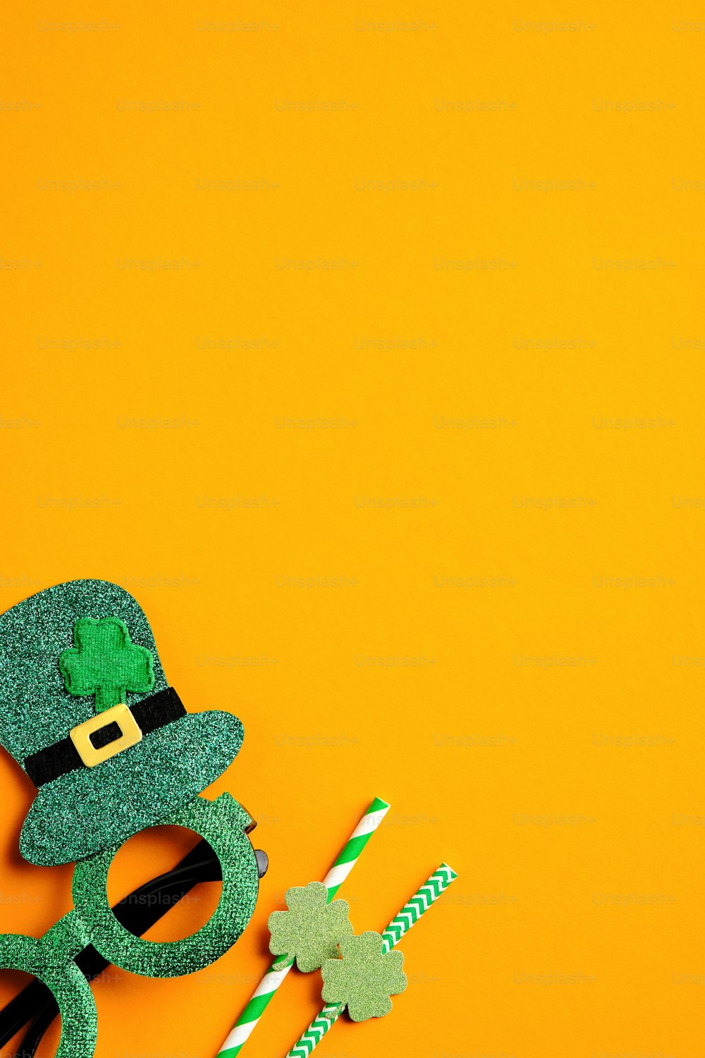 Saint Patrick's Day minimal concept. Festive party glasses and drinking straws on orange background. Flat lay, top view. Happy St Patricks Day banner design.