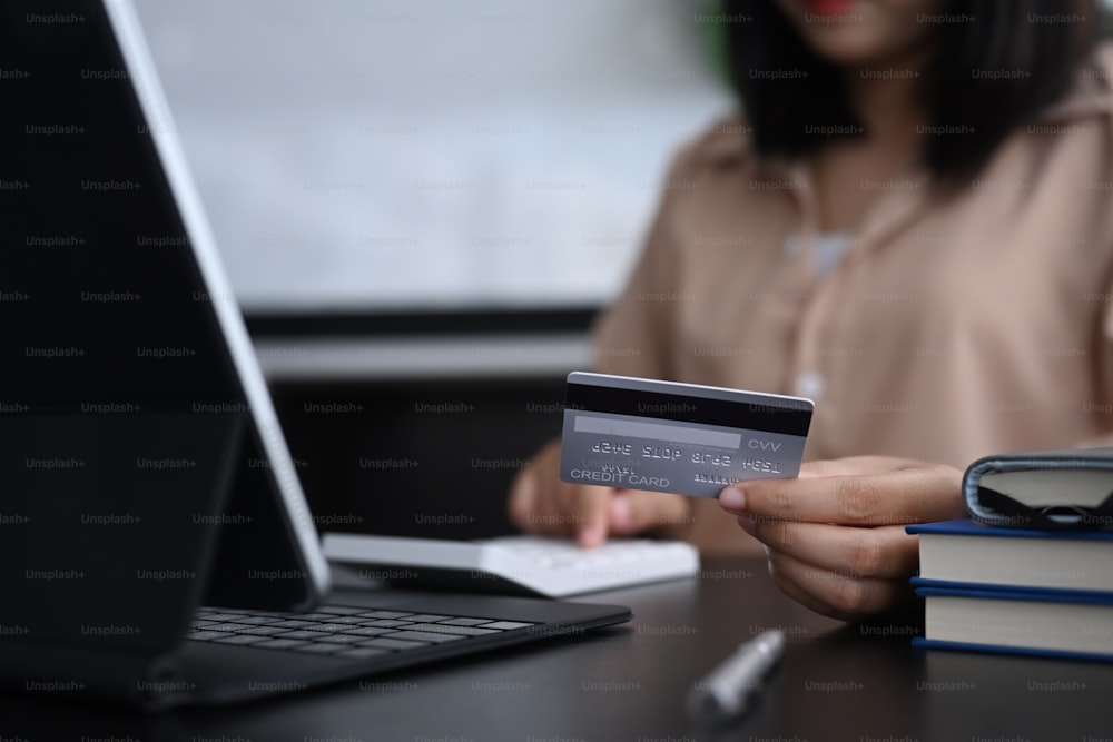 Young woman holding credit card and making calculations for online shopping or online payment.