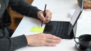Cropped shot of man working with computer tablet and making note on sticky note at his office desk.